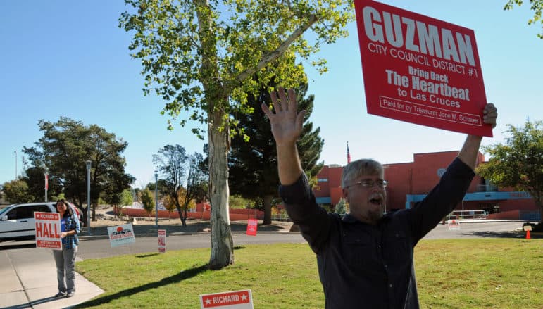 Las Cruces City Council District 4 candidate Richard Hall holds up a sign for a candidate for a different seat on the council, District 1's Eli Guzman, in front of the Branigan Library on Tuesday. Hall's wife Lupe stood nearby holding a sign promoting the candidacy of her husband.