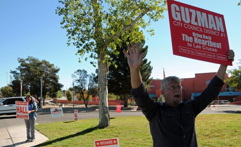 Richard Hall, a candidate for the District 4 seat on the Las Cruces City Council, holds a sign for a candidate running for a different council seat — District 1’s Eli Guzman — in front of the Branigan Library on Tuesday. Hall’s wife Lupe stands nearby holding a sign promoting her husband’s candidacy.